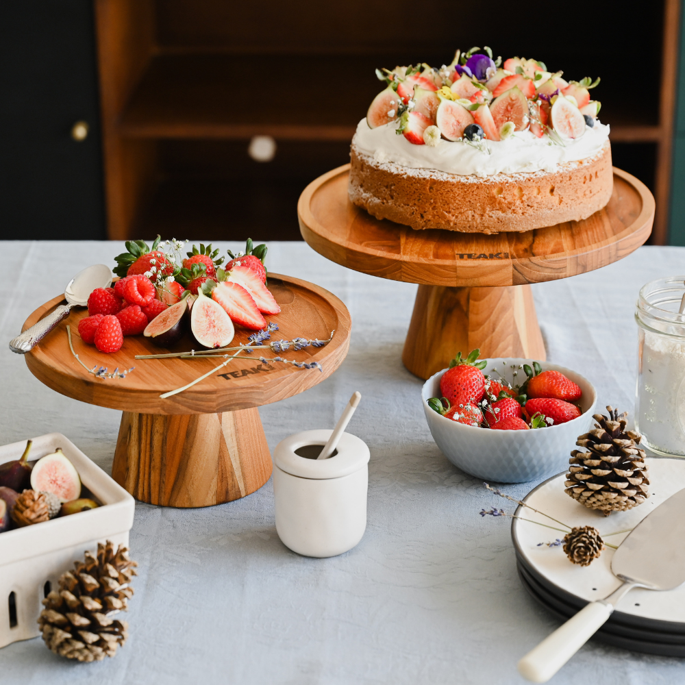 Elevated teakwood cake stands showcasing a fruit-topped cake and fresh berries in a traditional table setting.