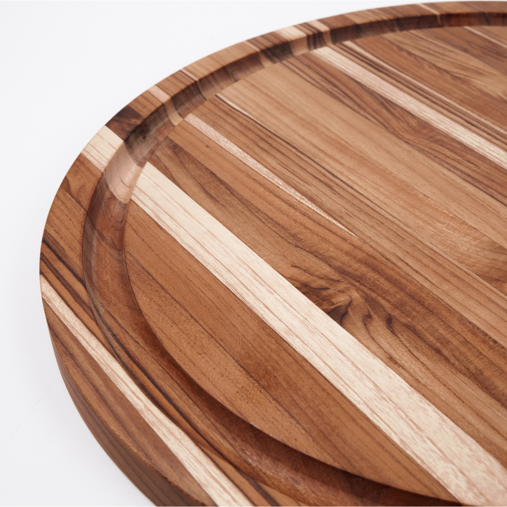 Close-up of a round teakwood carving board featuring a deep juice groove and natural edge grain patterns.