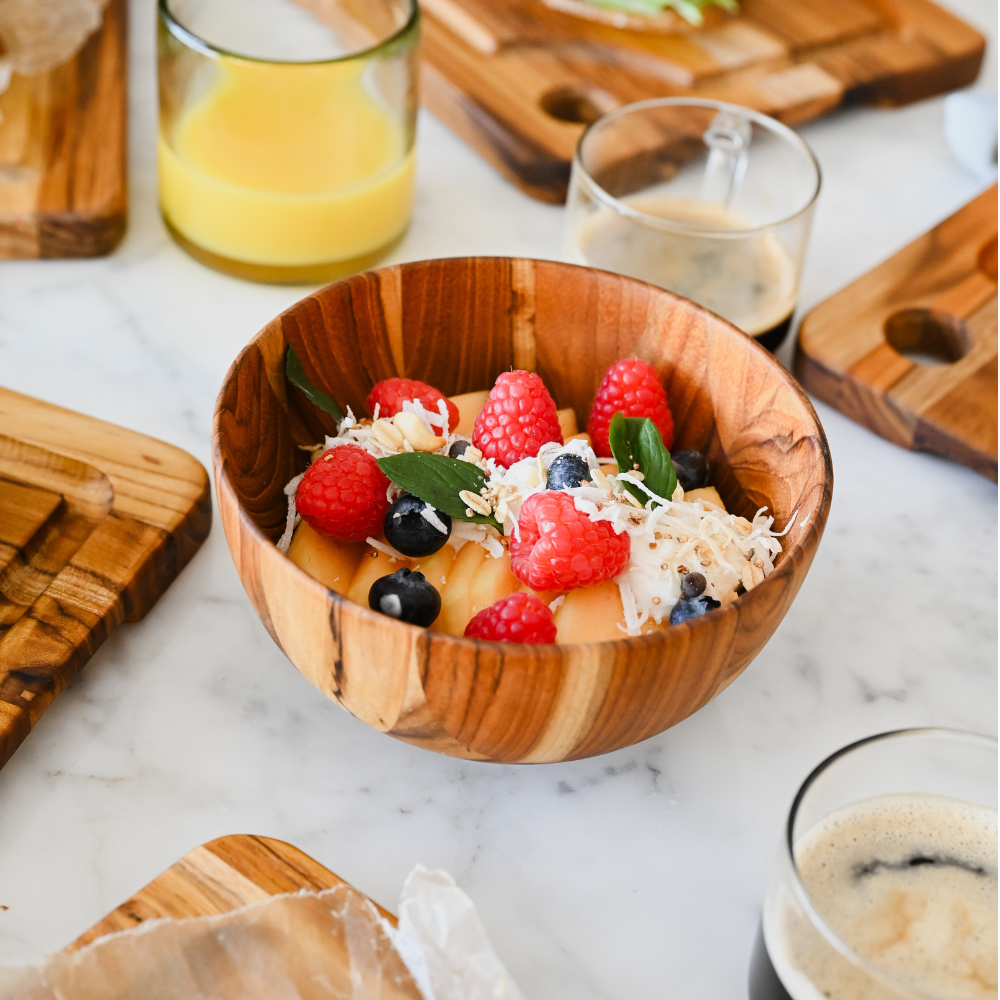 Round teakwood Moon Serving Bowl filled with fresh fruit and coconut in a lifestyle breakfast scene.