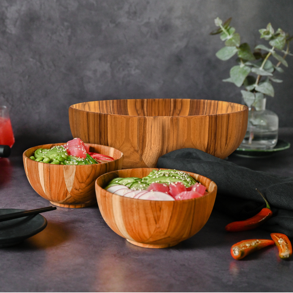 Large teakwood Moon Salad Bowl and matching smaller bowls with fresh ingredients on a dark stone surface.