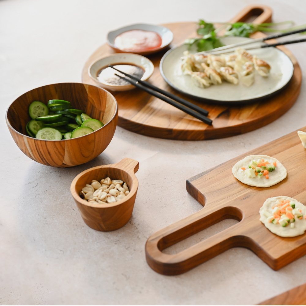 Small teakwood tapas bowl with handle, styled with peanuts and appetizers on natural teak serving boards.