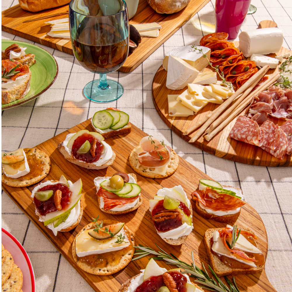 Teakwood serving boards featuring a variety of charcuterie and appetizers on a checkered tablecloth.