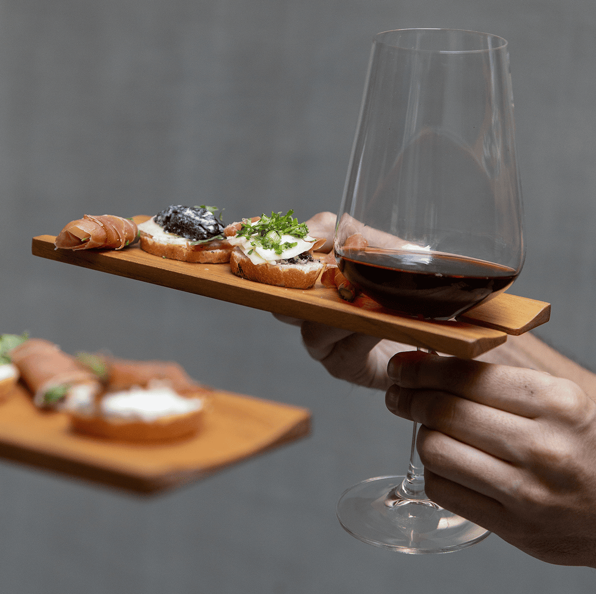 Teakwood wine and canape catering plate featuring gourmet appetizers and a slotted design to hold a wine glass.