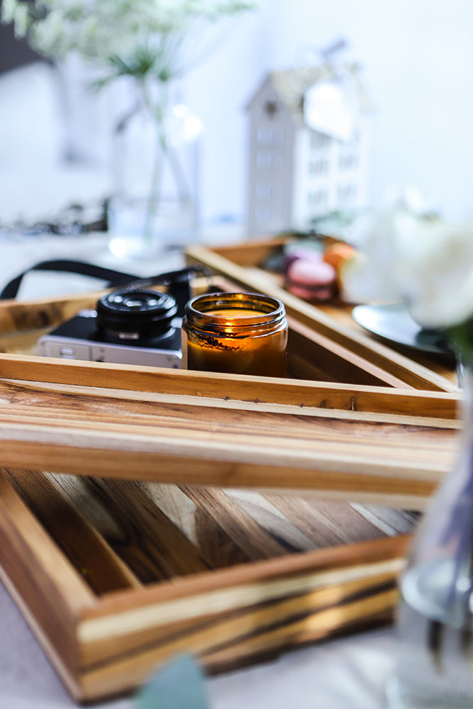 Nesting teakwood trays holding a vintage camera and lit candle in a bright lifestyle setting.