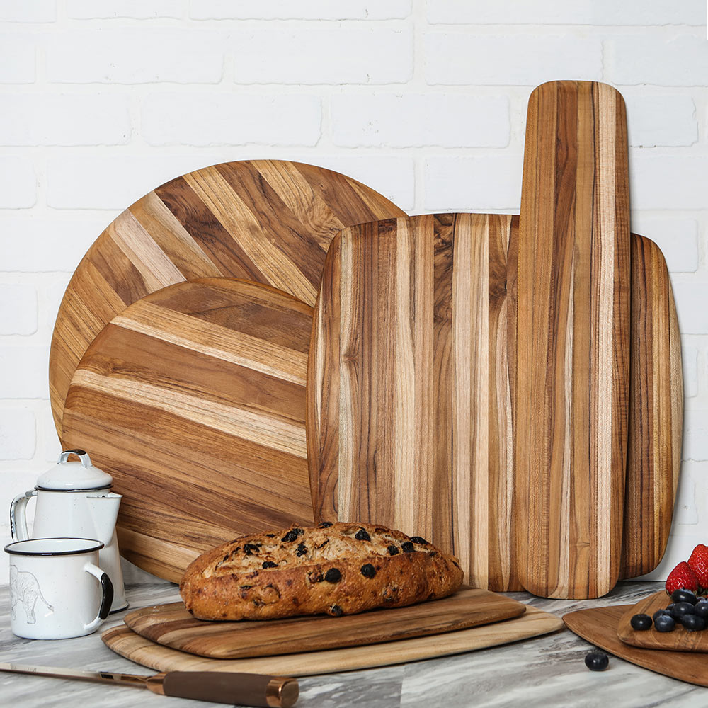 Teakwood cutting and serving boards with rounded edges displayed on a kitchen counter with fresh bread.