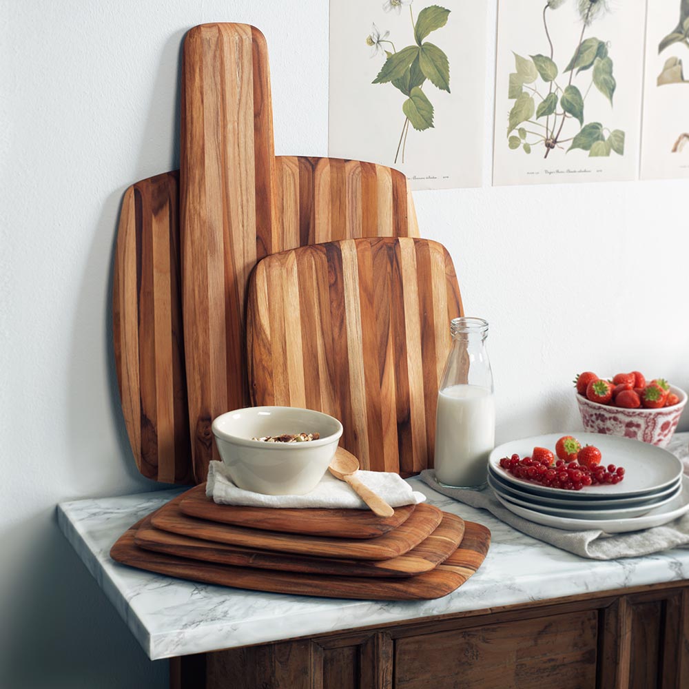 Teakwood serving boards with rounded edges arranged on a marble kitchen counter with fresh berries and breakfast.