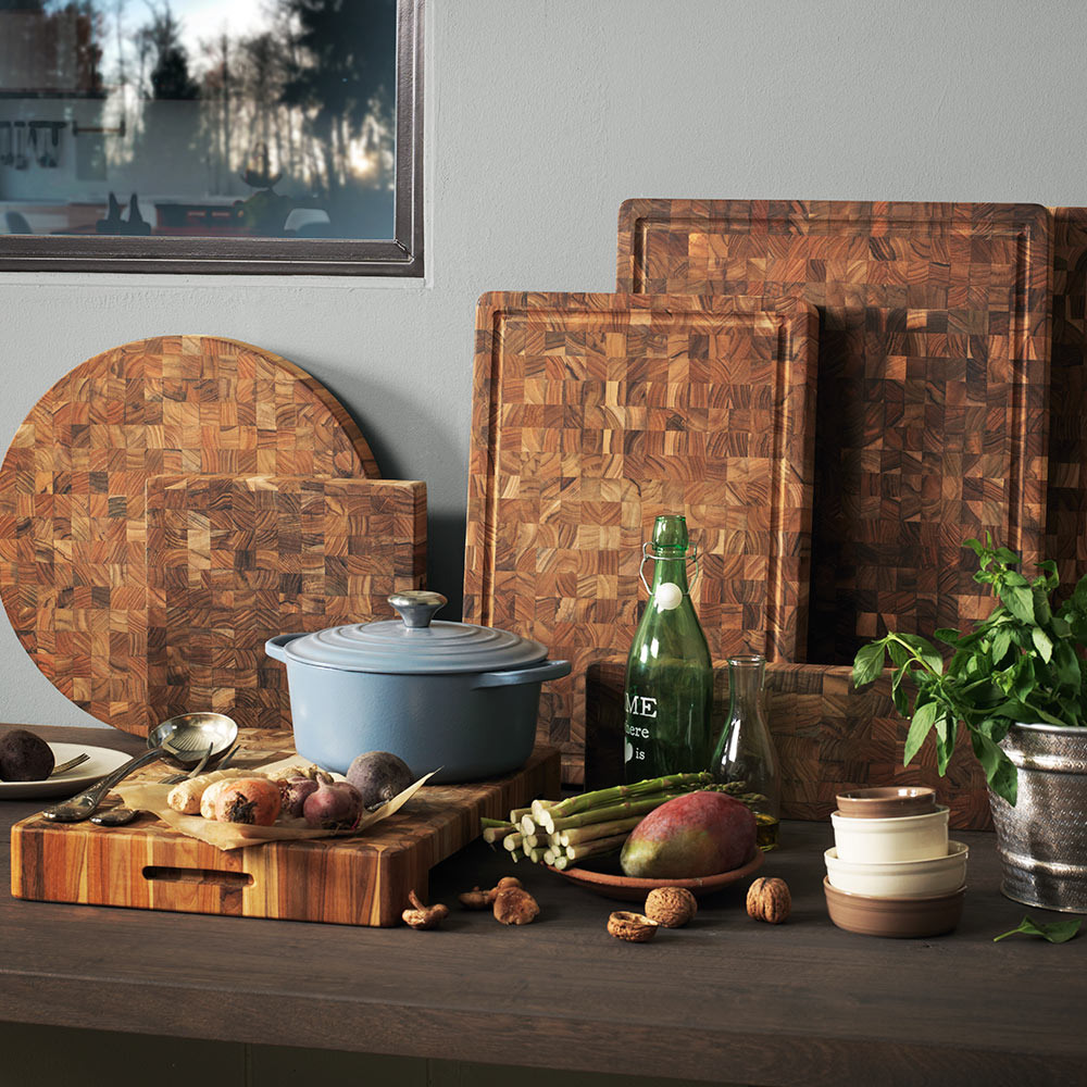 Thick end grain teakwood butcher block cutting boards in a kitchen with a blue Dutch oven and fresh vegetables.