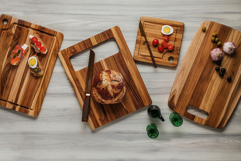 Marine edge grain teak chopping boards with hanging hole handles, styled with fresh bread and appetizers.