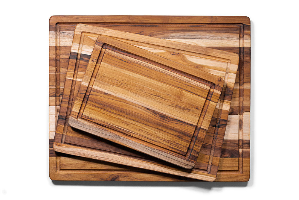 Three stacked rectangular teak wood cutting boards featuring natural edge grain and built-in juice canals.