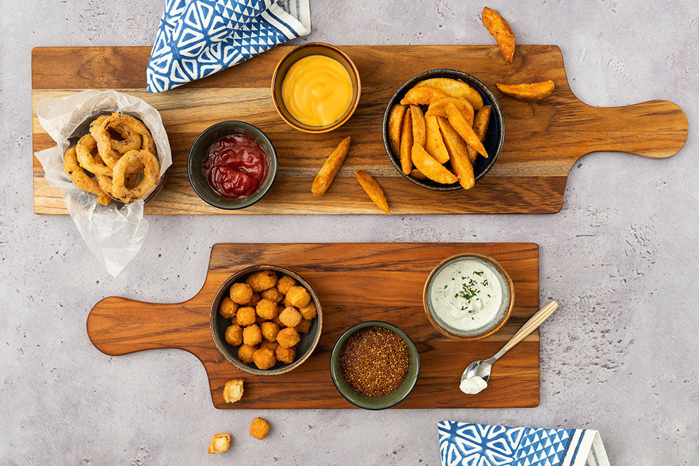 Teakwood paddle serving boards topped with fried appetizers and dipping sauces on a textured grey background.