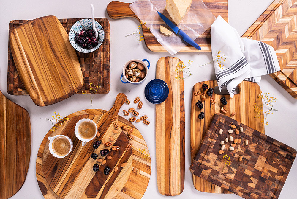Collection of teakwood serving and pizza boards in various shapes, styled with cheese, nuts, and fresh berries.