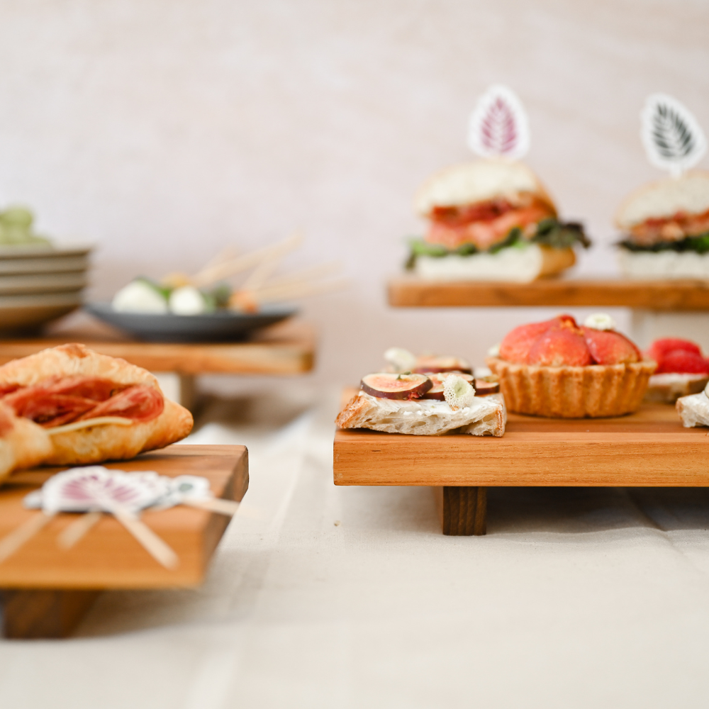 Elevated teakwood food stands showcasing a variety of sweet and savory appetizers in a serving display.
