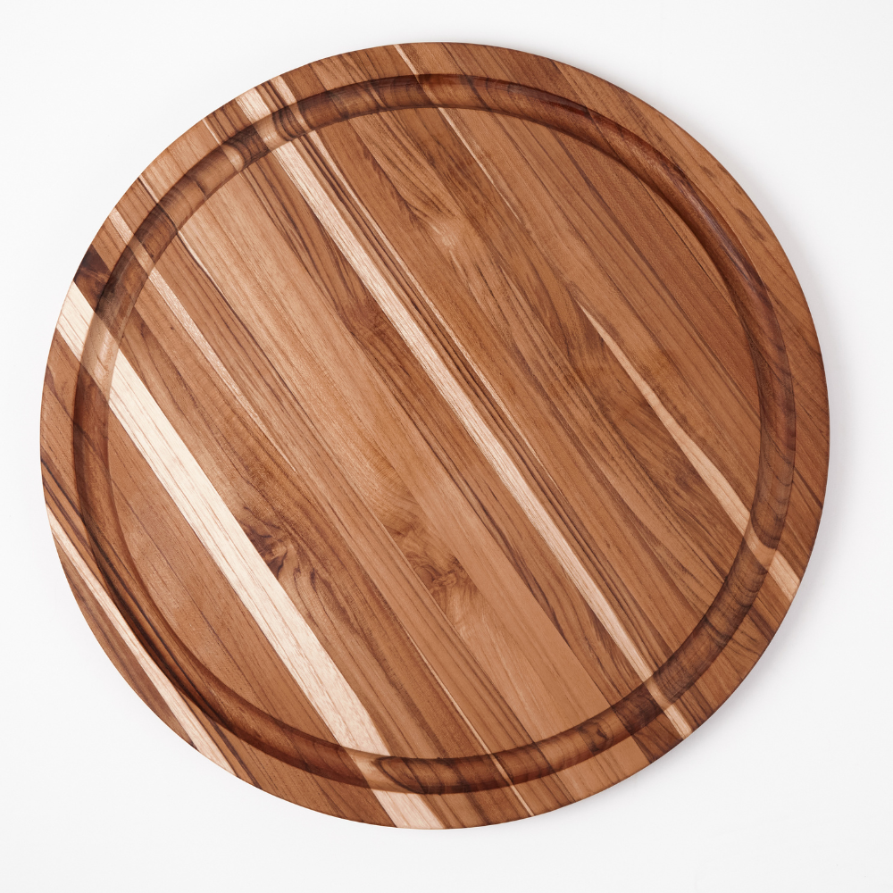 Scandi round teakwood carving board with edge grain patterns and a perimeter juice groove on white background.