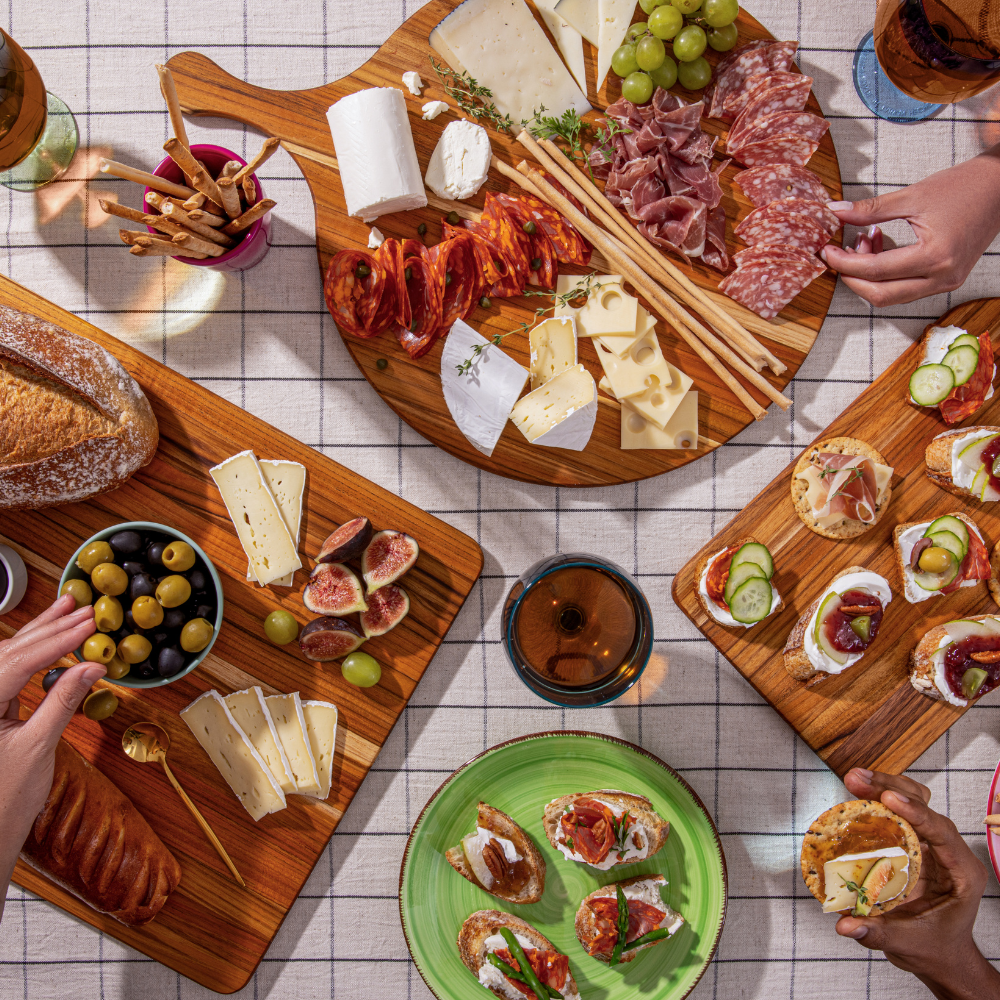 Three teakwood serving boards featuring round and rectangular designs with an elegant charcuterie spread.