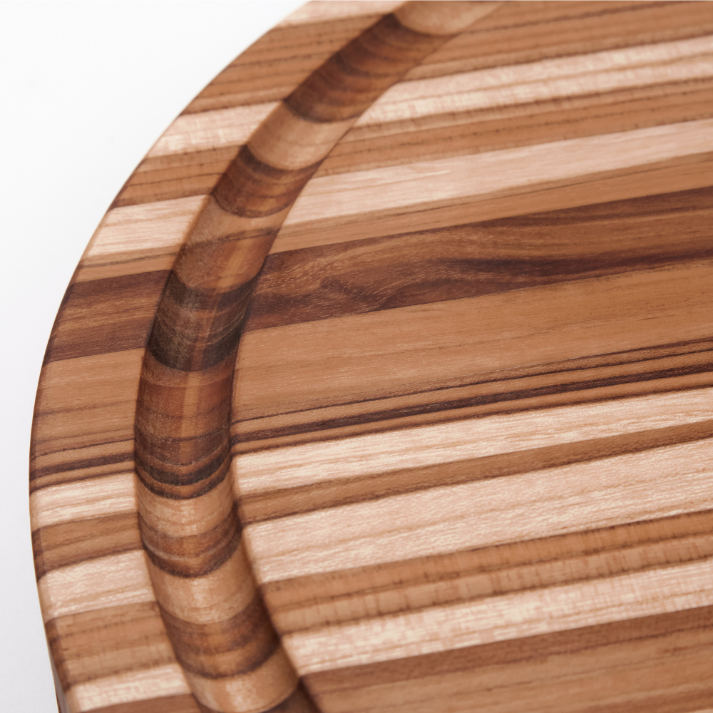 Round teakwood carving board detail highlighting the rich edge grain and integrated juice groove.