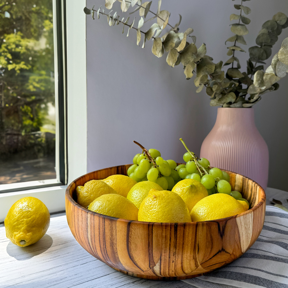 Large teakwood Moon Salad Bowl filled with lemons and green grapes, sitting on a white surface near a window.