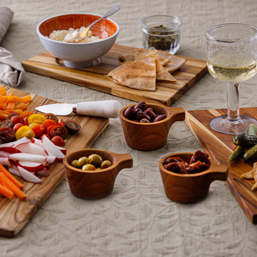 Small teakwood tapas bowls with handles filled with olives and snacks in a stylish lifestyle table spread.