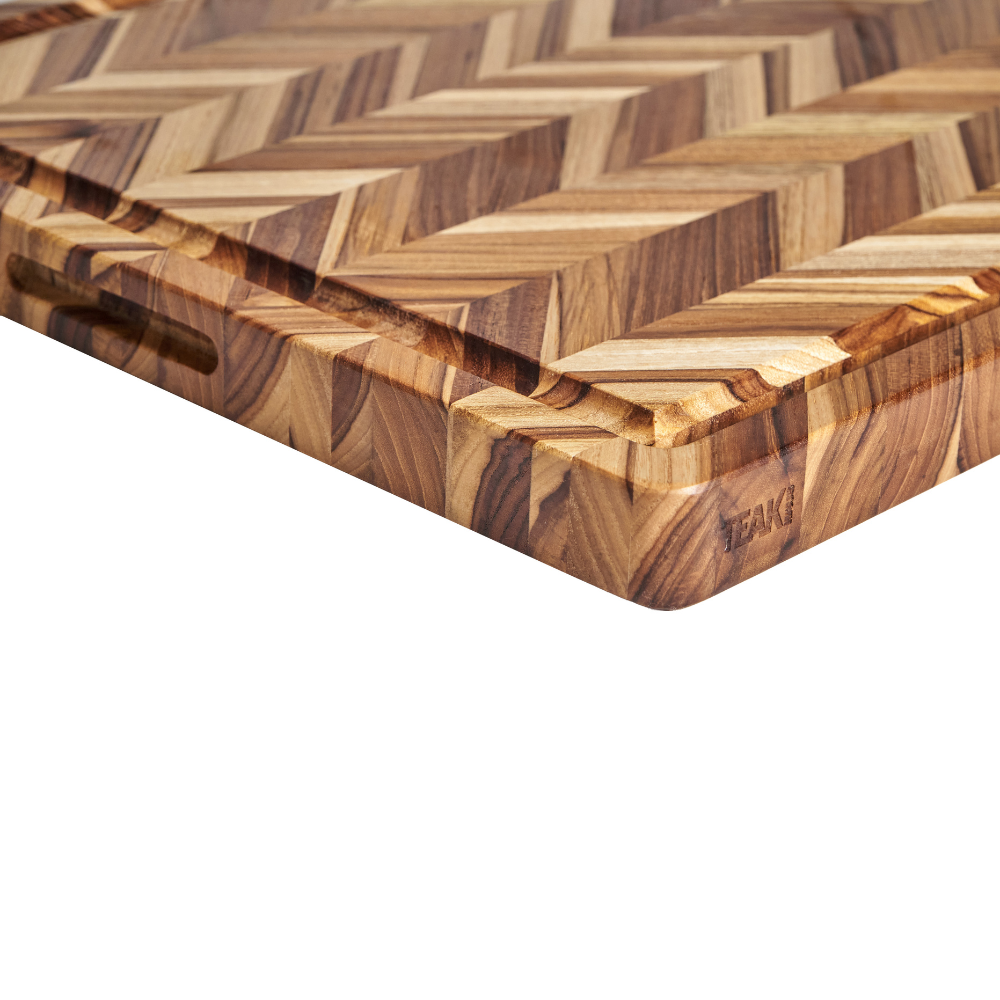 Close-up of a teakwood cutting board featuring a herringbone pattern, juice groove, and Teakhaus logo.