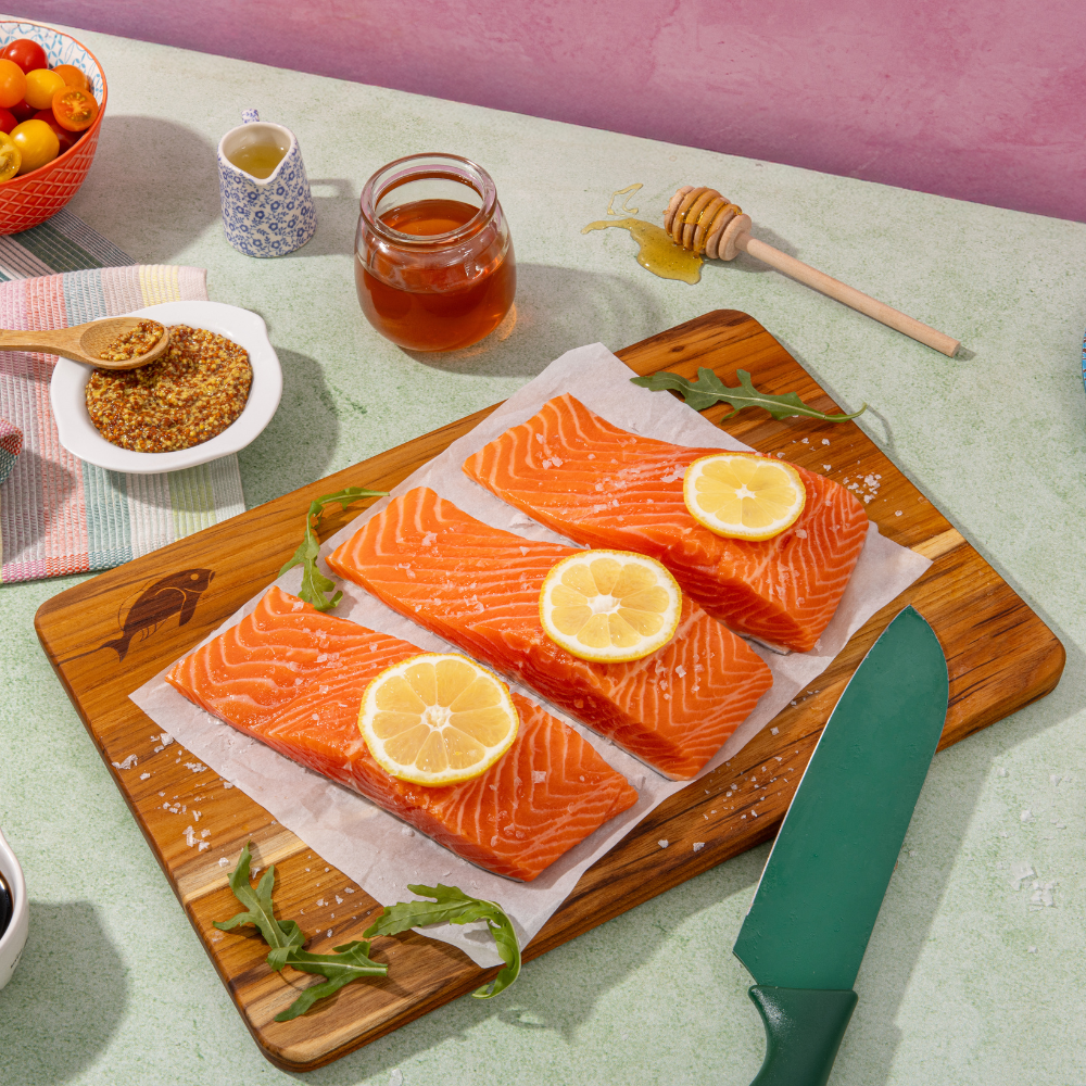 Rectangular teakwood cutting board featuring fresh salmon fillets with lemon slices for kitchen prep.
