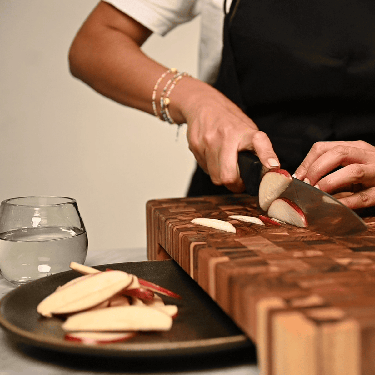 Extra-thick teak end-grain butcher block with a plate cutout, shown being used to slice red apples.