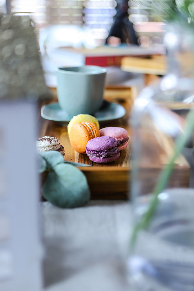 Small teakwood serving tray holding colorful macarons and a coffee cup in a cozy lifestyle setting.