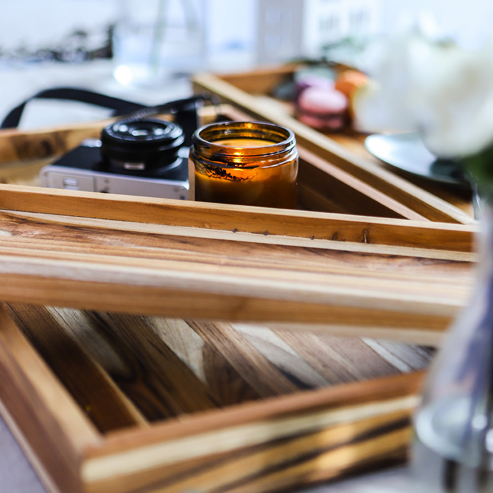 Nesting rectangular teakwood trays in an edge grain finish holding a lit candle and camera.