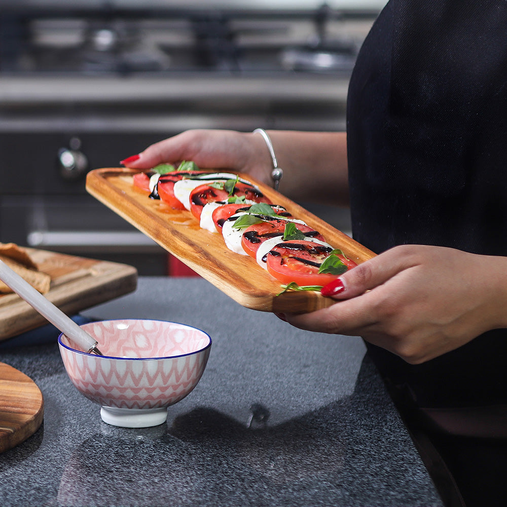 Rectangular teakwood serving tray held by hands, featuring a fresh caprese salad with balsamic glaze.