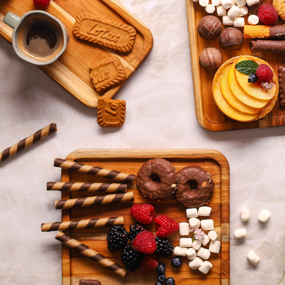 Small square teakwood serving trays holding a variety of berries, chocolates, and coffee for a dessert display.