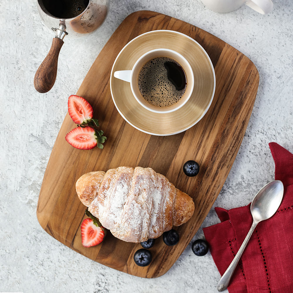 Small teakwood serving board featuring a croissant, berries, and coffee cup on a light textured background.