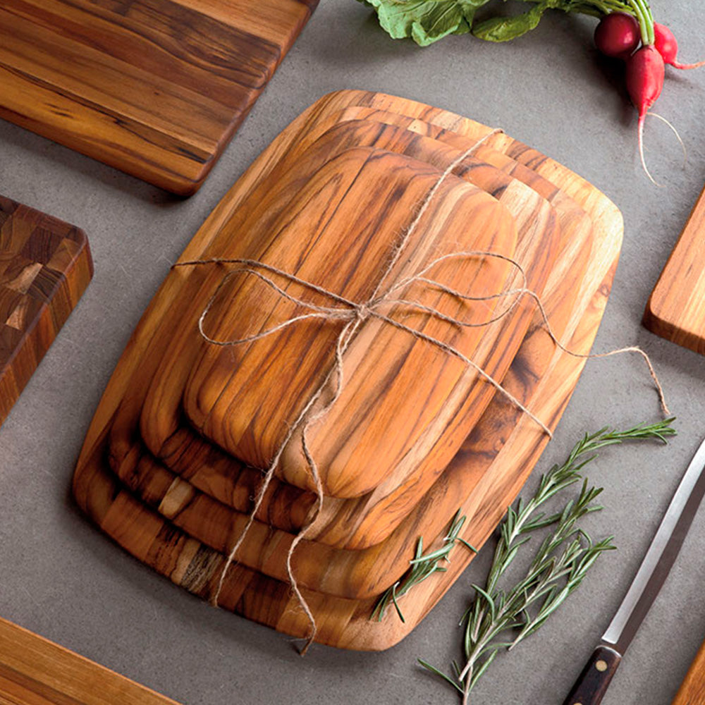 Four stacked teak wood serving boards with rounded edges and rich edge grain tied with a rustic twine bow.