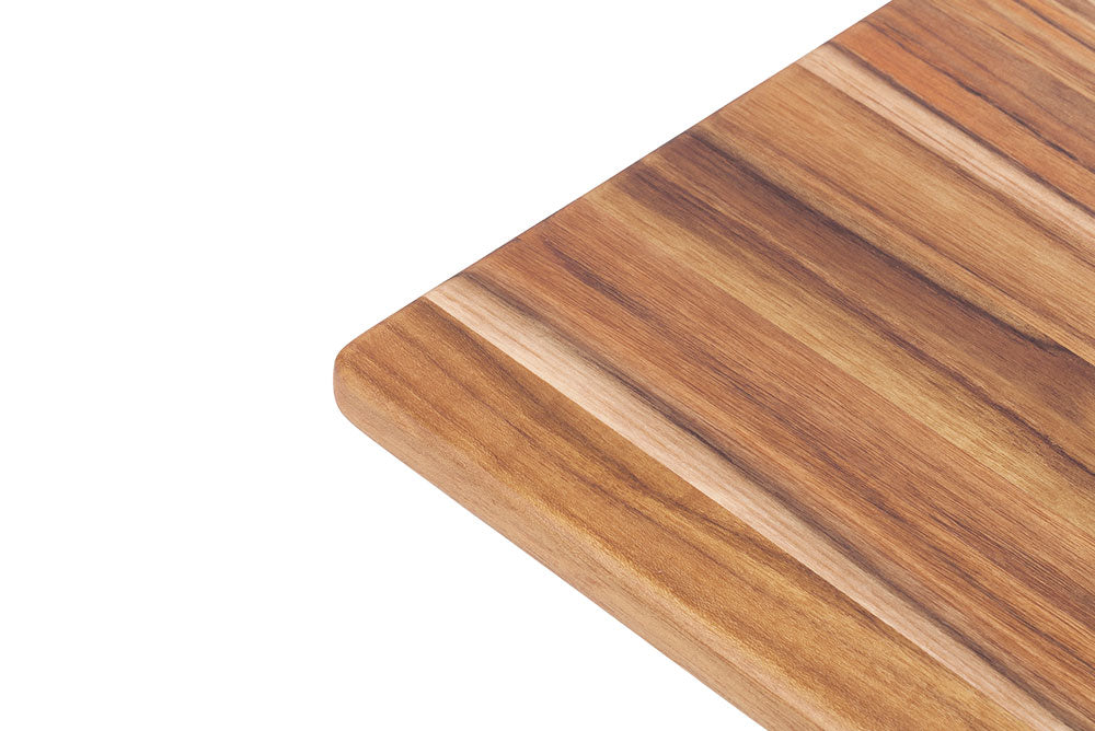 Close-up corner of a rectangular edge grain teakwood cutting board showing natural wood grain patterns.