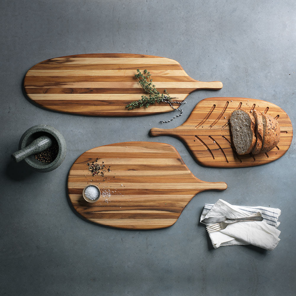 Sustainable teak wood paddle serving boards in various shapes, including the long 703 canoe model, on a grey surface.