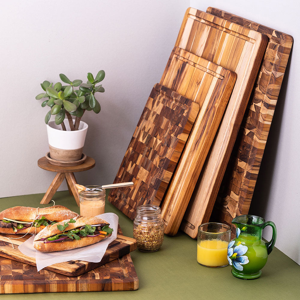 Sustainable teakwood cutting boards with edge and end grain patterns displayed in a kitchen with prepared food.