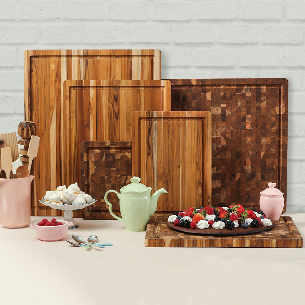 Teak wood cutting boards in edge and end grain styles, displayed with a berry tart and kitchen accessories.
