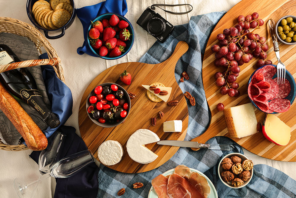 Round teakwood Atlas Pizza Serving Board featured in a charcuterie spread with cheese and fruit.